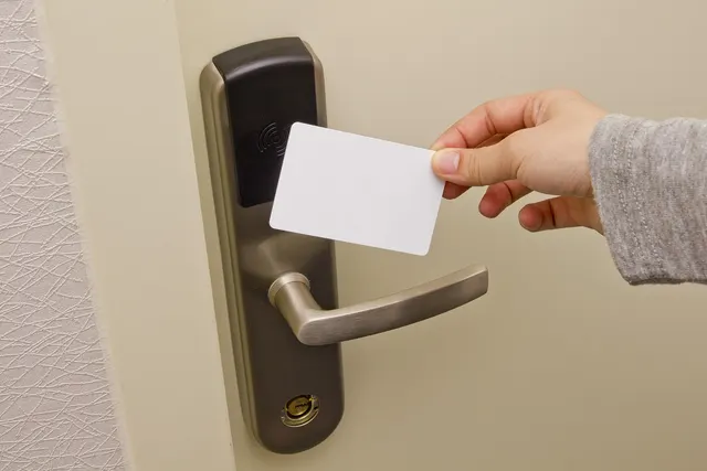 Hand holding a blank white key card up to an RFID reader on an electronic door lock with a metal lever handle