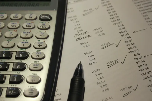 Scientific calculator and black pen resting on a printed financial statement with handwritten checkmarks and notes