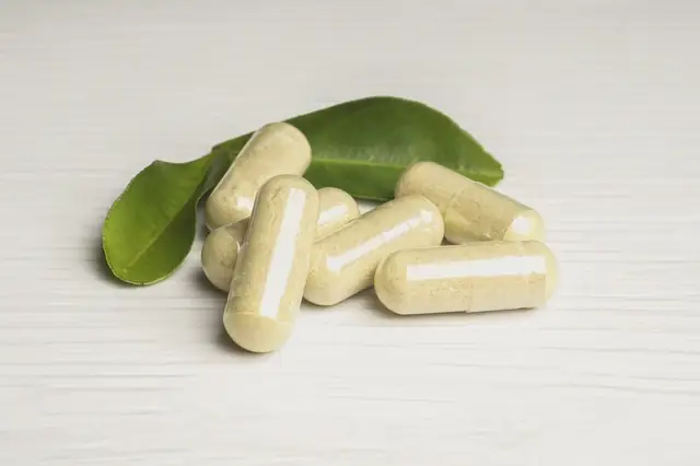 Pale green herbal capsules next to a fresh green leaf on white