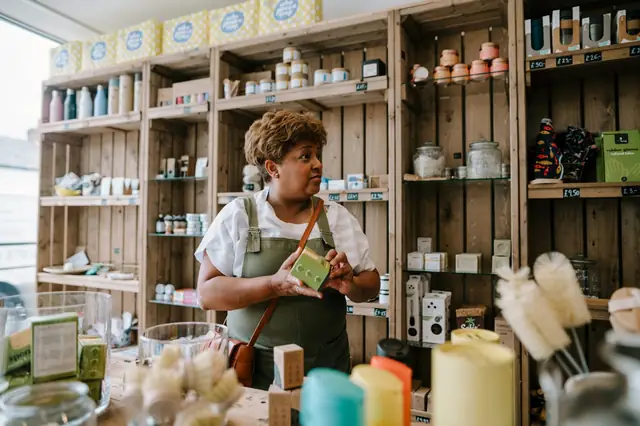 Shop owner holding a soap bar in a refill store with wooden shelves
