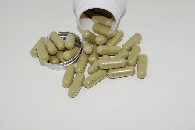 Green herbal powder capsules spilling from a white supplement bottle beside a round metal lid on a white surface