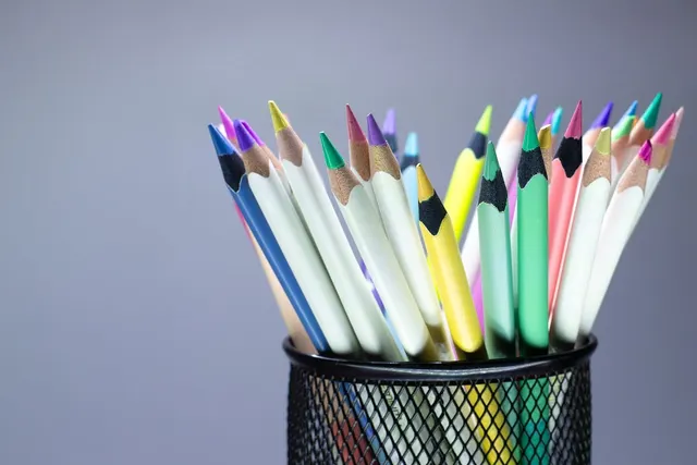 Sharpened colored pencils in pastel and bright shades standing in a black mesh desk holder against a gray background