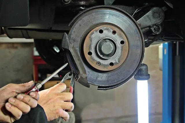 Mechanic's hands using a screwdriver and pliers on a car's brake disc and caliper bracket in an auto repair shop