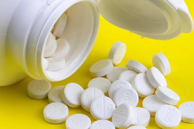 White tablets spilling from an open white plastic bottle onto a bright yellow surface
