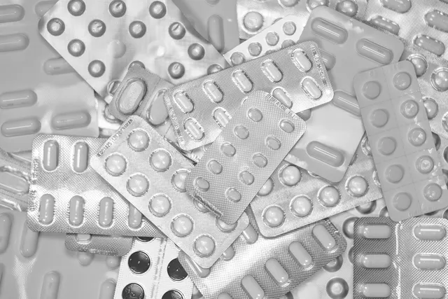 Black-and-white pile of foil blister packs holding assorted prescription tablets and capsules
