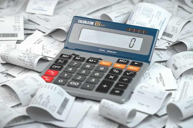 Gray desktop calculator showing zero on top of a large pile of printed paper sales receipts