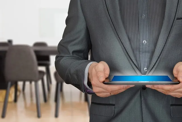 Businessman in a gray pinstripe suit holding a tablet with a glowing blue screen in a modern conference room
