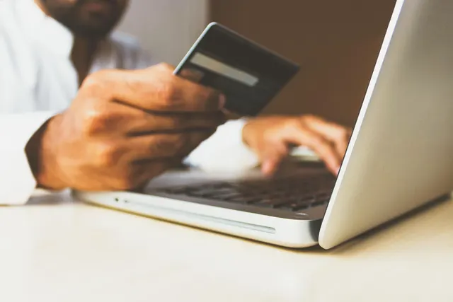 Man holding a credit card in one hand while typing on a silver laptop keyboard at a white desk