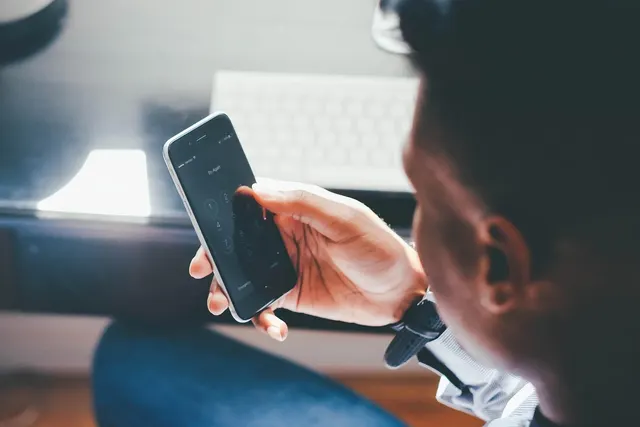 Over-the-shoulder view of a person entering a passcode on a smartphone keypad near a desk with a white keyboard