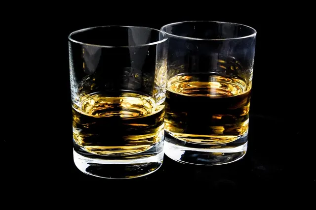 Two rocks glasses partly filled with amber bourbon whiskey against a black background