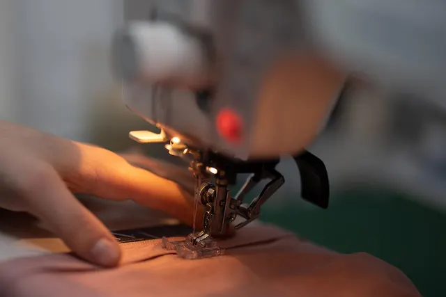 Close-up of hands guiding pink fabric under a sewing machine needle and presser foot during a garment alteration