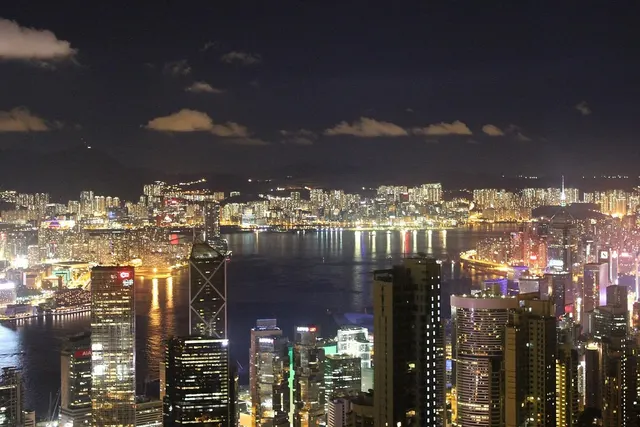 Hong Kong skyline at night seen from above, with lit skyscrapers lining Victoria Harbour and Kowloon beyond