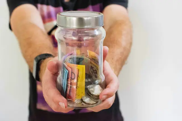 Hands holding a glass jar filled with banknotes and coins