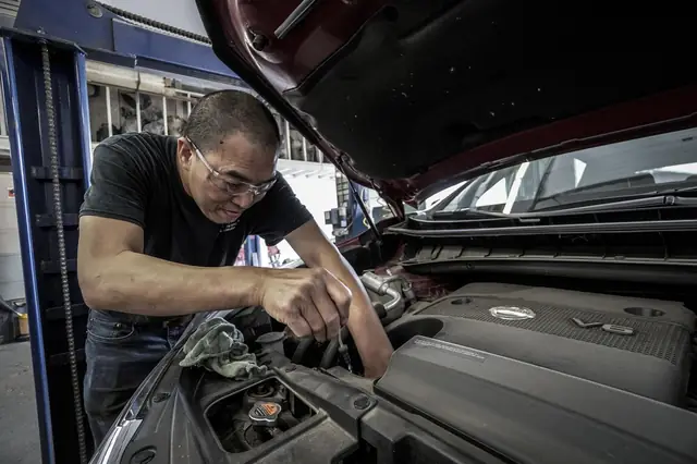 Mechanic leaning under an open car hood, working on the engine