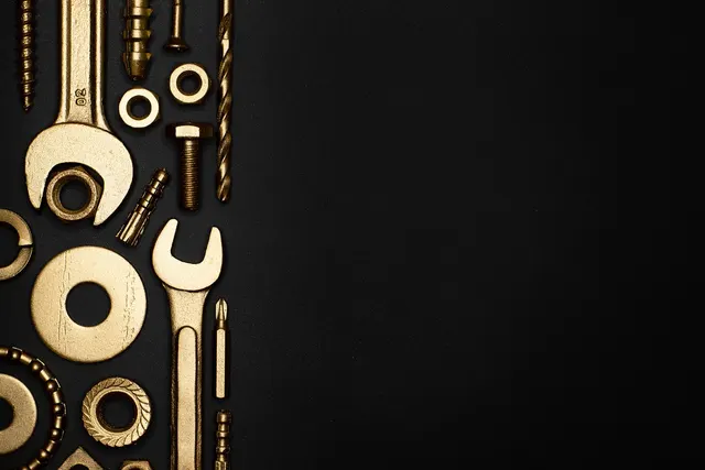 Gold-colored wrenches, bolts, nuts, washers, screws and a drill bit arranged in a flat lay on a black background