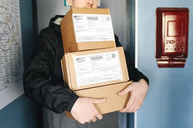Courier carrying three stacked cardboard shipping boxes through a doorway