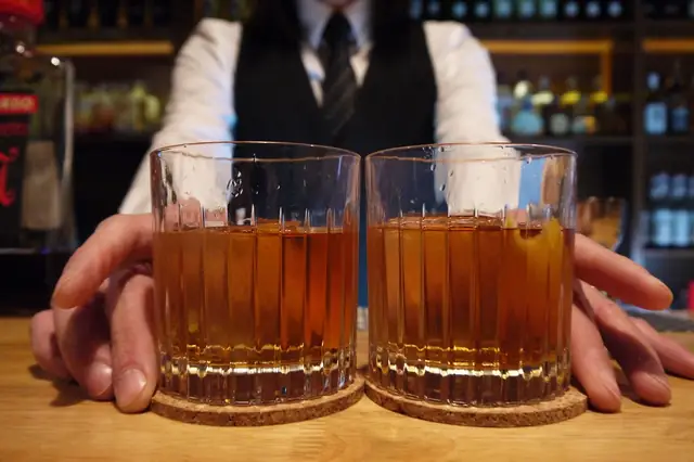 Bartender sliding two glasses of whiskey across a wooden bar