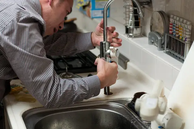 Plumber working under a kitchen faucet beside the sink
