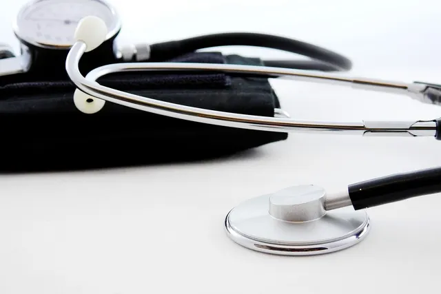 Close-up of a silver stethoscope resting beside a black blood pressure cuff and gauge on a white surface