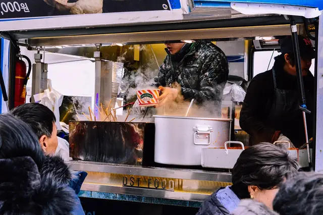 Cooks serving steaming food from a street stall to waiting customers