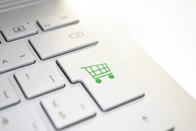 Close-up of a white laptop keyboard with a green shopping cart icon on the enter key, suggesting online checkout