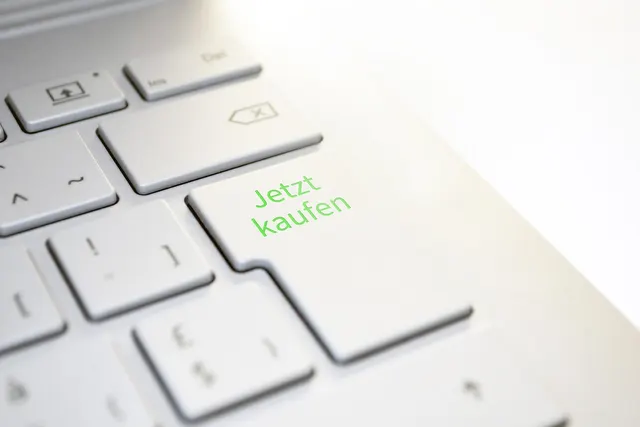 Close-up of a silver laptop keyboard with the enter key relabeled 'Jetzt kaufen' (Buy now) in green letters
