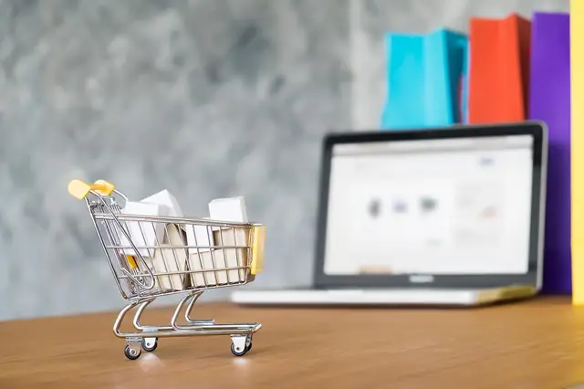 Miniature shopping cart beside a laptop and colorful shopping bags