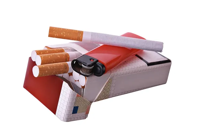 Open red and white cigarette pack with cigarettes sticking out, a red lighter and a loose cigarette on top, on white