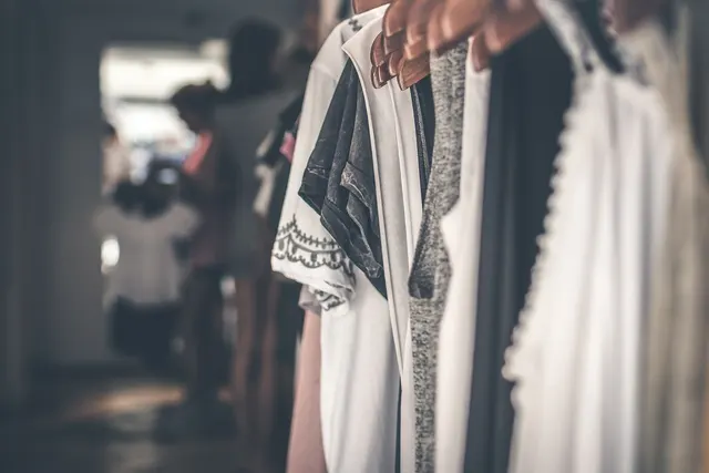 Close-up of white, gray and black shirts on wooden hangers in a small clothing boutique, shoppers blurred behind