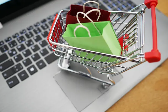 Miniature shopping cart holding green and red paper shopping bags on a silver laptop keyboard