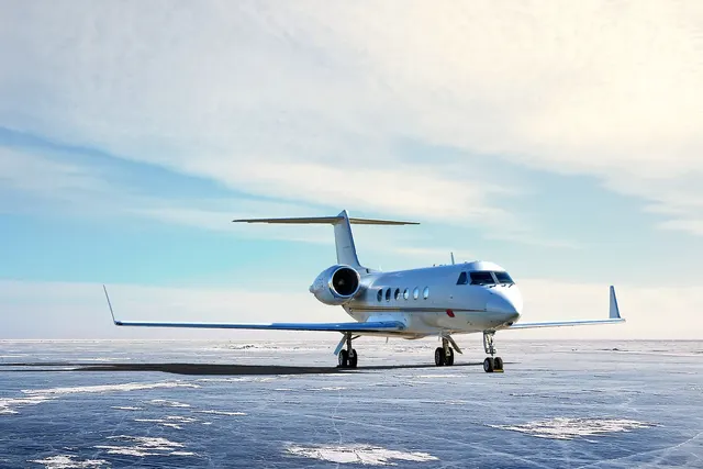 White private business jet parked on a frozen, snow-dusted icy surface under a pale blue winter sky