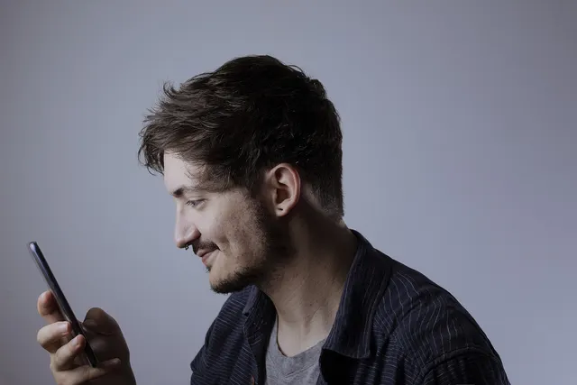 Smiling young man with a beard in a pinstripe shirt looking at his smartphone against a plain gray background