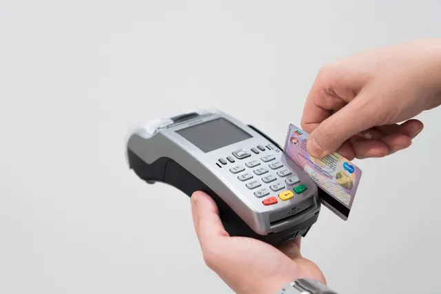 Hands swiping a credit card through the magnetic stripe reader of a handheld card payment terminal on a white background
