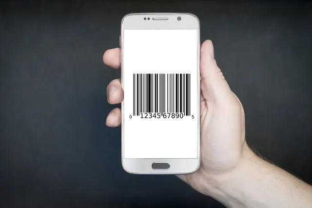 Hand holding a white smartphone displaying a barcode on its screen against a dark gray background