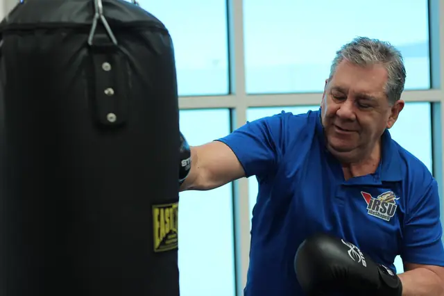 Smiling man in a blue polo punching a heavy bag in a gym