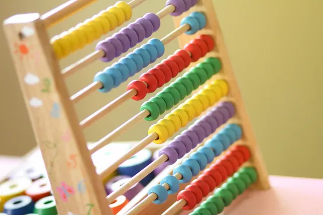 Colorful wooden toy abacus with rows of beads on a table in a childcare classroom, with stacking toys behind it