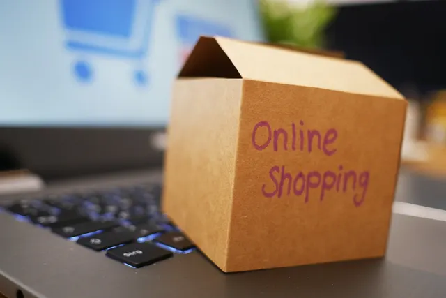 Small cardboard box hand-labeled Online Shopping on a laptop keyboard, shopping cart icon on the blurred screen