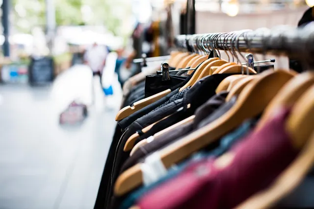 Rack of secondhand jackets and tops on wooden hangers outside a clothing shop, with a blurred street behind