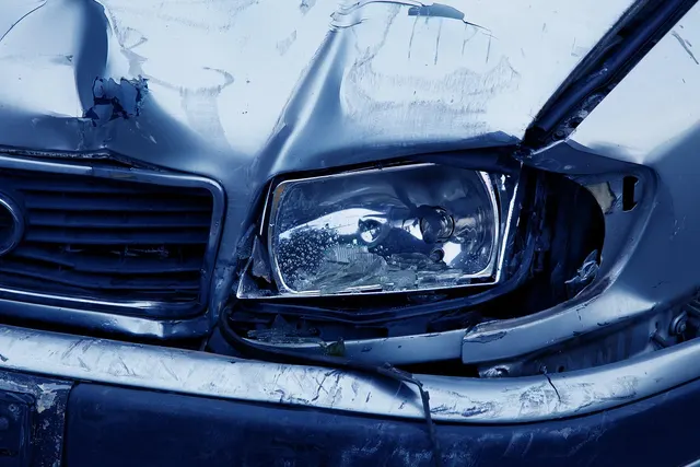 Close-up of a damaged silver car front with a crumpled hood, cracked headlight and dented bumper awaiting repair