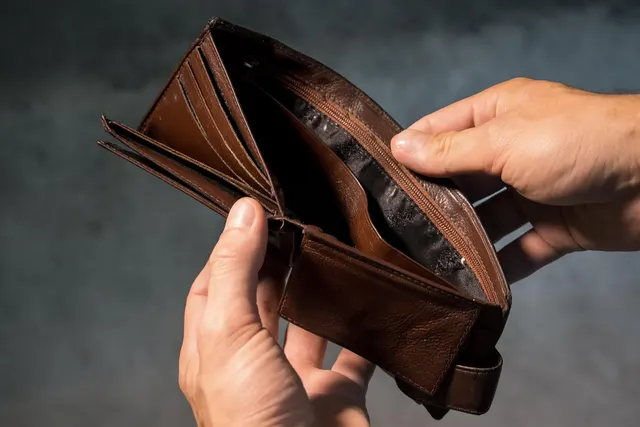 Hands holding open an empty brown leather wallet against a dark gray background
