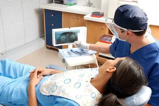 Dentist in mask and visor treating a patient lying in the dental chair