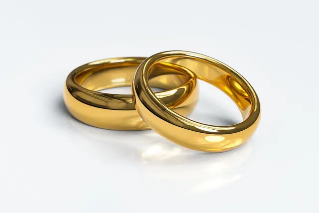 Two polished gold wedding bands resting together on a white reflective surface