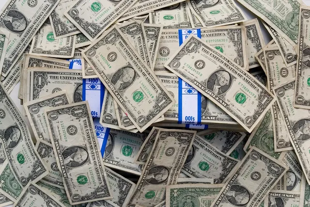 Pile of scattered US one-dollar bills with several bundles wrapped in blue-and-white $100 currency straps