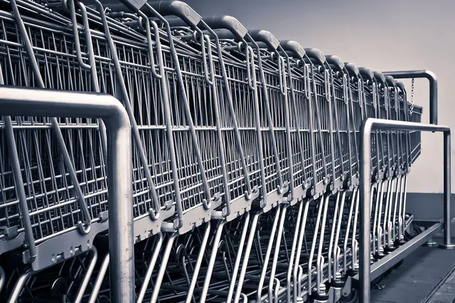 Row of nested metal shopping carts lined up beside a steel railing outside a store, in desaturated tones