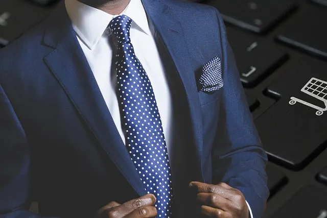 Businessman in navy suit and polka-dot tie overlaid on a dark laptop keyboard with a shopping cart key