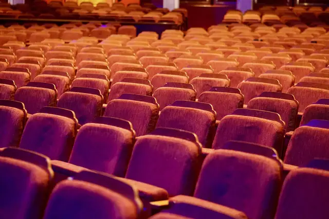 Rows of empty red auditorium seats under warm stage lighting