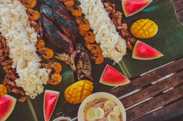 Feast of rice, grilled fish, shrimp and fruit spread on banana leaves