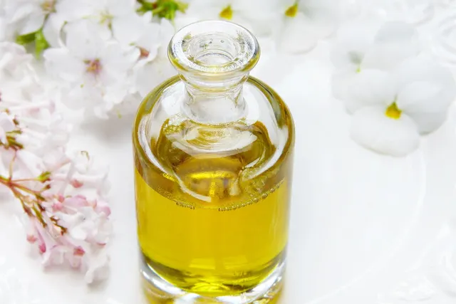 Clear glass bottle of golden oil on a white surface surrounded by white and pale pink blossoms