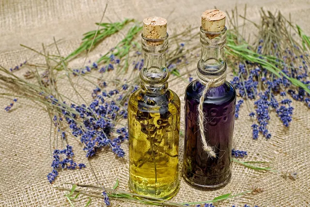 Two cork-stoppered glass bottles of yellow and purple herbal oil on burlap surrounded by dried lavender sprigs