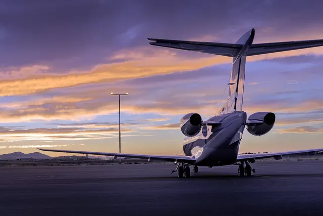 Private business jet parked on an airport tarmac at sunset, viewed from behind under a purple and orange sky